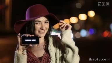 快乐的购物妇女在时尚的帽子显示智能手机与特别优惠购物夜在晚上的黑屏